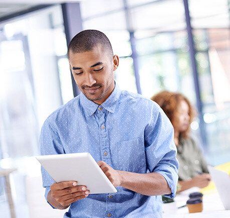 Smiling businessman uses a tablet with his coworker in the background