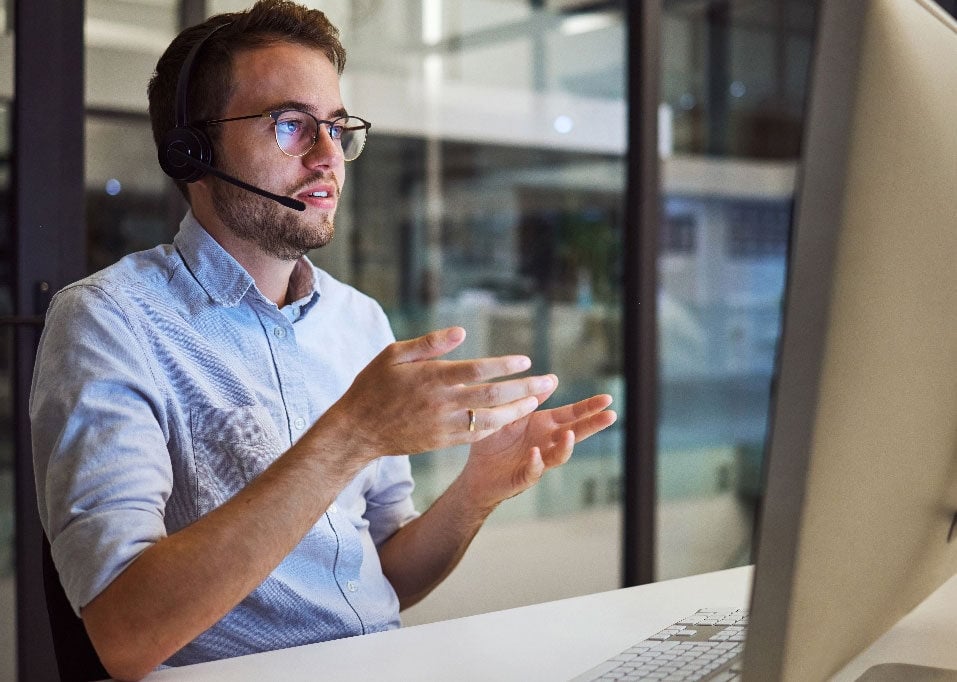 Man looking at computer screen with hands out and wearing a headset